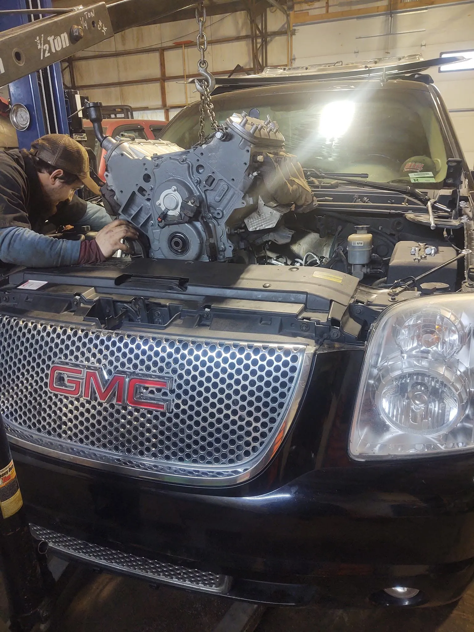 A technician guiding a replacement engine into a GMC SUV with an engine hoist inside the Battle Creek Diesel shop